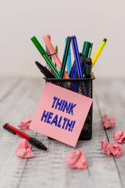 Think Health 'i gösteren bir not yazıyorum. Tamamen fiziksel ve sosyal refahın olduğu iş fotoğraflarının gösterilmesi. Ahşap masa üzerinde boş çarşaf ve kağıt kırıntıları olan yazma ekipmanları..