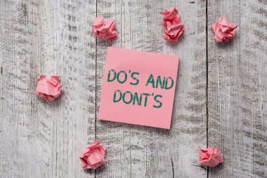 Do S is and Don 't S is' i gösteren bir not yazıyorum. İş fotoğraflarında, ahşap desenli masa kırıntıları içeren basit not kağıtlarıyla ilgili kurallar ve gelenekler gösteriliyor..