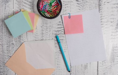 Front view open colored rectangular envelope blank sheet paper stacked sticky note pads ballpoint clips holder lying retro vintage rustic old lumber timber table background.