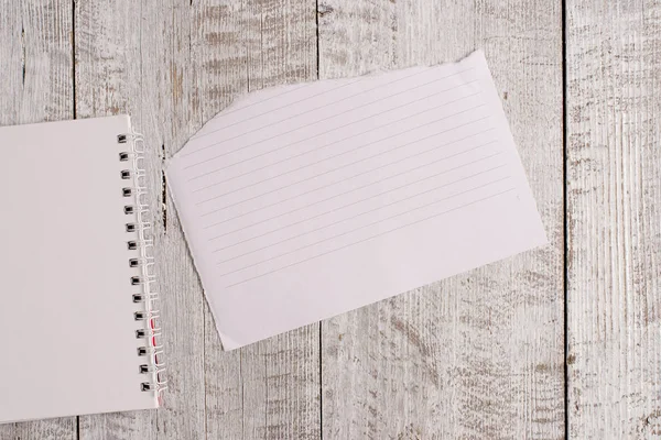 Rozdarty papier i notebook arkusz umieszczony na szczycie drewnianego stołu. Papery stacjonarne trzymać się klasyczne tło w pozycji pochył. Artystyczny sposób płaskiego lay fotografii — Zdjęcie stockowe