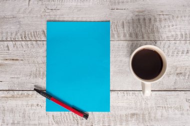 Ahşap arka planda kahve fincanının yanına ekipman yazmak. Masanın üstündeki bardağın yanına boş kağıt koyulmuş. Dairenin düzenlenmesinde sanatsal yol fotoğrafçılıktır