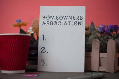 Handwriting text writing Homeowners Association. Concept meaning Organization with fee for upkeeps of Gated Community Flowers and stationary plus plain sheet with paper big cup above a table. clipart