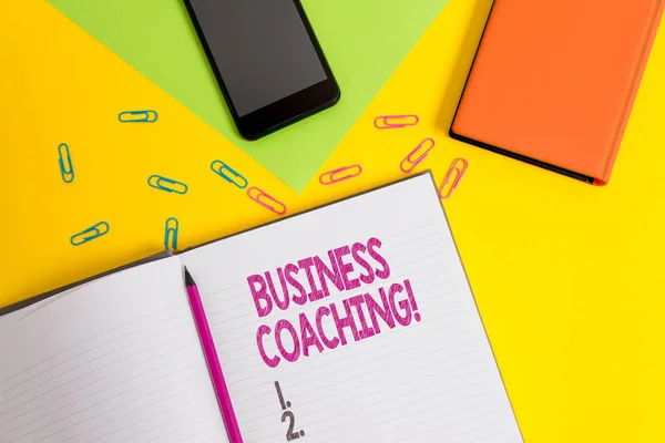 Texto de caligrafia Business Coaching. Conceito significado Ajudar os funcionários a se tornarem mais ativos Consultoria de um especialista Clipes de lápis de folha de papel em branco smartphone dois blocos de notas fundo colorido . — Fotografia de Stock