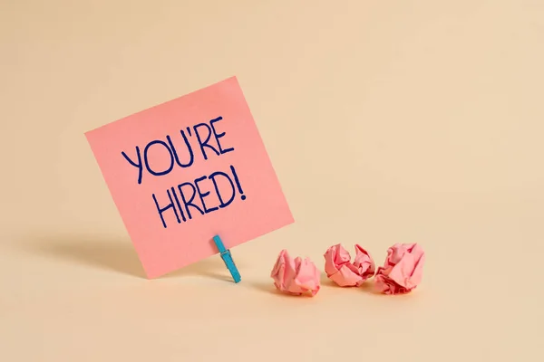 Handwriting text You Re Hired. Concept meaning Used by huanalysis resources indicate employee that he is got job Plain note paper and stationary placed above soft pastel colour backdrop. — Stock Photo, Image