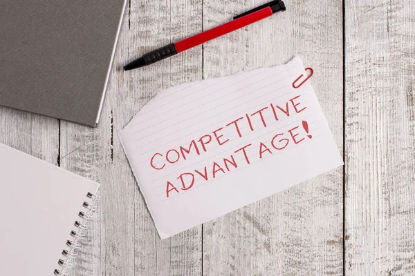 Handwriting text Competitive Advantage. Concept meaning Company Edge over another Favorable Business Position Torn paper and notebook sheet with a pen placed on top of wooden table.