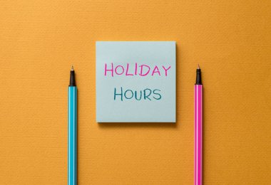 Text sign showing Holiday Hours. Conceptual photo employee receives twice their normal pay for all hours Front view blank colored sticky note two ballpoints cool yolk background.