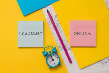 Learning Online'ı gösteren metin işareti. Kavramsal fotoğraf Internet ve teknoloji Yardımı ile yeni bir şey öğrenin Not Defterleri kalem renkli kağıt levhalar çalar saat ahşap arka plan.