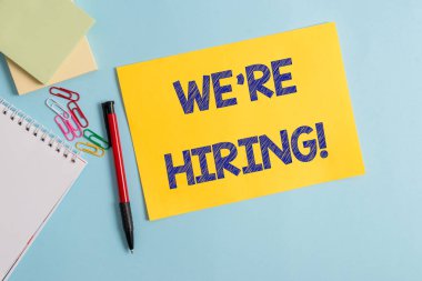 İşe Aldığımızı gösteren bir not yazıyorum. Başvurularıgözden geçirme ve adayları bulma işlemi İş fotoğraf vitrine Düz karton ve pastel renk zemin üzerine yerleştirilen yazma ekipmanları.