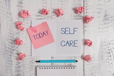 Öz Bakım'ı gösteren bir metin işareti. Kavramsal fotoğraf bir geliştirmek için harekete geçme uygulaması kendi sağlık Kareli spiral not defteri küçük not aparat vurgulayıcı kağıt topları ahşap arka plan.