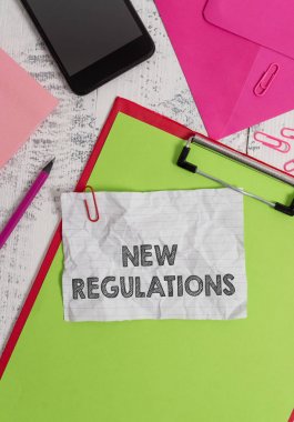 Yeni Düzenlemeleri gösteren kavramsal el yazısı. Genellikle kurallar tarafından kullanılan etkinliği kontrol eden Yönetmelik'i gösteren iş fotoğrafı. Pano levha kalem akıllı telefon klipleri not defteri ahşap arka.