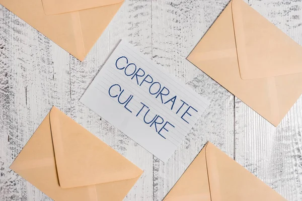 Text sign showing Corporate Culture. Conceptual photo pervasive values and attitudes that characterize a company Four envelopes around ruled paper sheet old wooden vintage background.