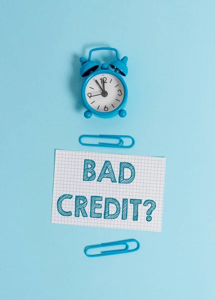 Handwriting text writing Bad Creditquestion. Concept meaning inabilityof a demonstrating to repay a debt on time and in full Alarm clock wakeup squared blank paper sheet clips colored background.