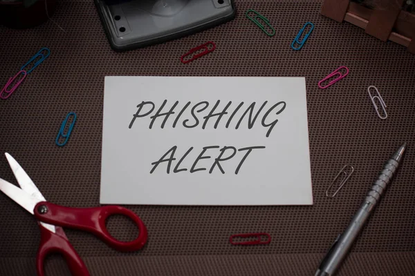 Handwriting text writing Phishing Alert. Concept meaning aware to fraudulent attempt to obtain sensitive information Scissors and writing equipments plus plain sheet above textured backdrop.