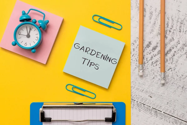 Writing note showing Gardening Tips. Business photo showcasing Proper Practices in growing crops Botanical Approach Notepads paper sheet clipboard markers alarm clock wooden background.
