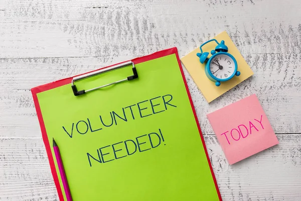 Handwriting text Volunteer Needed. Concept meaning need work for organization without being paid Metal clipboard sheets marker alarm clock notes pad wooden background.