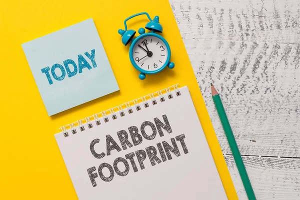 Text sign showing Carbon Footprint. Conceptual photo amount of dioxide released atmosphere result of activities Spiral notepad paper sheet marker alarm clock retro wooden background.