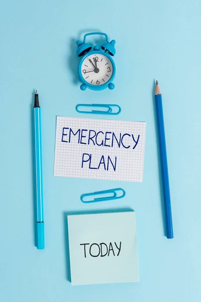 Writing note showing Emergency Plan. Business photo showcasing Procedures for response to major emergencies Be prepared Alarm clock squared paper sheet notepad markers colored background.