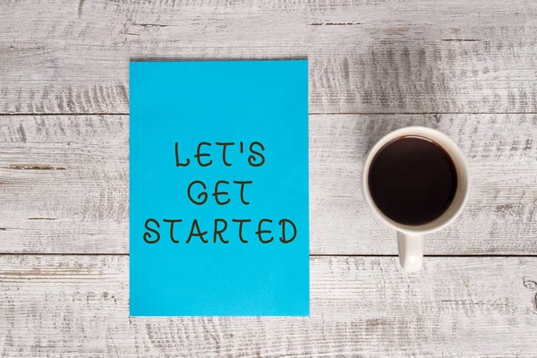 Conceptual hand writing showing Let S Is Get Started. Business photo text to begin doing or working on something you had started Stationary placed next to a coffee cup above wooden table.