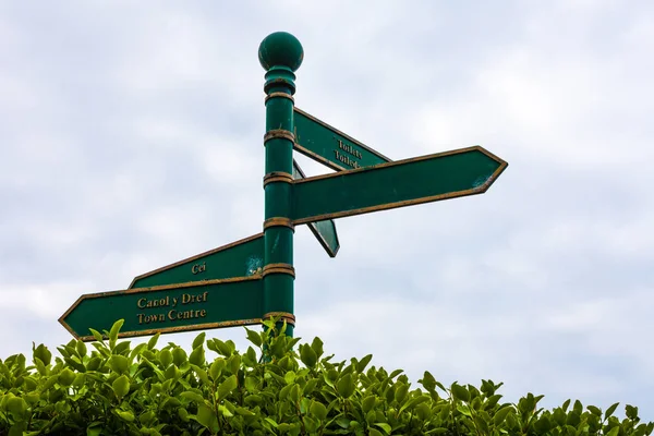 Green road sign on the crossroads with blue cloudy sky and green grass in the background. Traveling concept with crossroad sign with blue and green background.