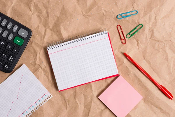 Mesa feita de papel artesanal amassado com um caderno vermelho espiral de papel quadrado aberto e eletrodomésticos de escritório. Mesa de papelaria com papéis e material de estudo. — Fotografia de Stock