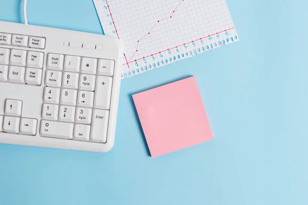 Light blue desk with empty paper notes, computer keyboard and office appliances. Blank space on reminders. Notebook papers and a chart in a square sheet with numbers.