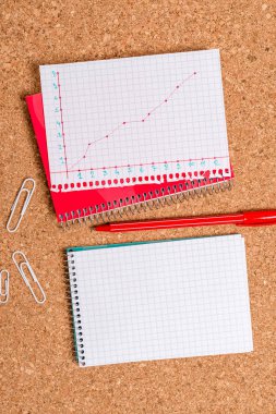 Açık kareli, sarmal bir not defteri ve ofis aletleri olan mantar masası. Farklı boyutlarda ve tipte kağıtları olan ilan masası, rakamlarla ve çalışma malzemeleriyle dolu bir tablo..