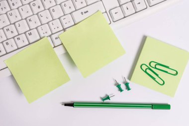 Beyaz arka plan ve bilgisayar klavyesi üzerinde kalem ataş ile Yeşil not kağıt. Metin mesajları için boş not kağıdının üzerine düz döşeme.