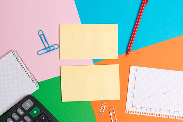 Colorful desk with different sizes and types of empty papers, office appliances and study supplies. Table made of pink, blue, green and orange squares paper with sticker note. — Stock Photo, Image