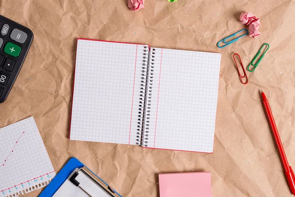 Mesa feita de papel artesanal amassado com um caderno vermelho espiral de papel quadrado aberto e eletrodomésticos de escritório. Mesa de papelaria com papéis e material de estudo. — Fotografia de Stock