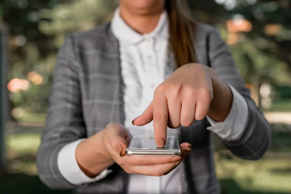 Woman in grey suites holds mobile phone. Business concept with business woman holding mobile phone with touch screen.