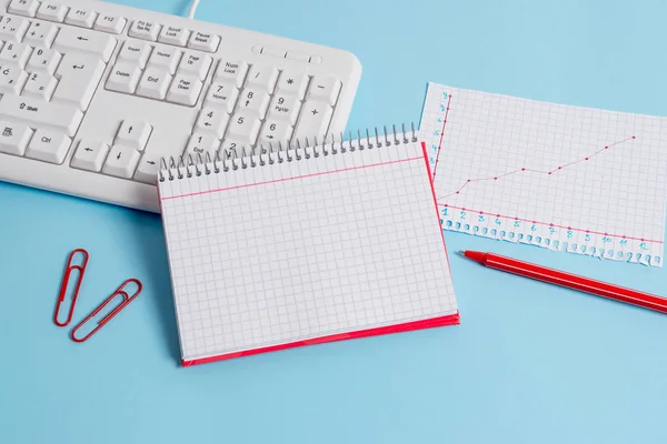 Light blue desk with empty paper notes, computer keyboard and office appliances. Blank space on reminders. Notebook papers and a chart in a square sheet with numbers.