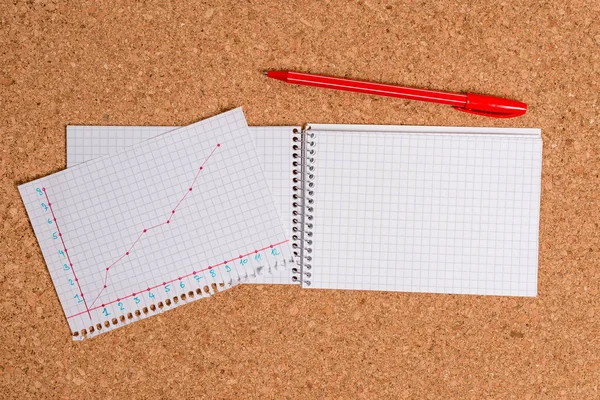 Corkboard Schreibtisch mit einem offenen quadratischen Papierspirale Notizbuch und Bürogeräten. Billboard-Tisch mit verschiedenen Größen und Arten von Papieren, eine Tabelle mit Zahlen und Studienmaterial. — Stockfoto