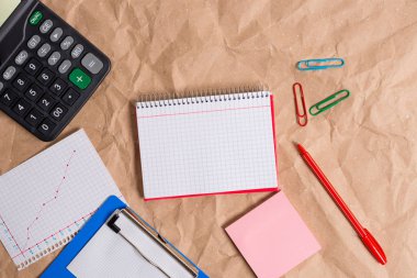 Buruşmuş el işi kağıdından yapılmış bir masa. Açık kare, sarmal, kırmızı bir defter ve ofis aletleri. Kağıt masası, kağıtlar ve çalışma malzemeleri..