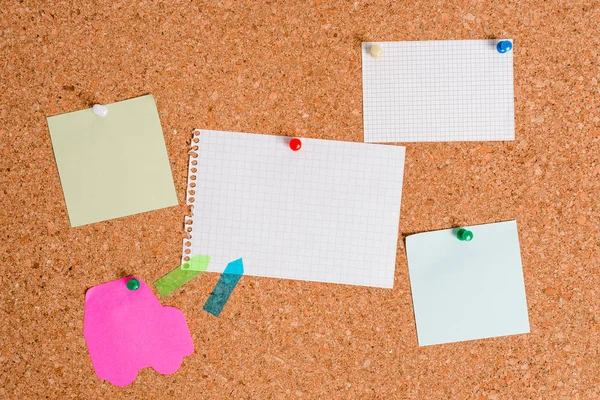 Corkboard met verschillende kleuren en afmetingen papier bevestigd door een pin. Rechthoek en vierkante platen op een billboard geplakt door gekleurde duimspijkers. prikbord met lege herinneringsnota. — Stockfoto