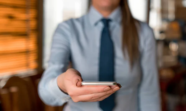 Mujer borrosa en el fondo sosteniendo el teléfono móvil en la mano. Copie el espacio con el dedo apuntando en él. Mujer de negocios con camisa y corbata en el fondo . —  Fotos de Stock