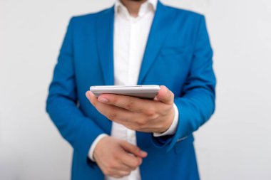 İşadamı elinde tur üst tutar. Dokunmatik ekranlı cep telefonu tutan adam ile iş konsepti. Mavi süitteki işadamı elinde cep telefonuyla duruyor.