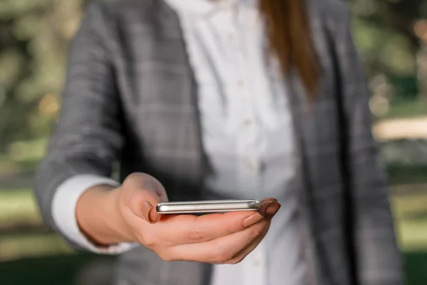 Woman in grey suites holds mobile phone. Business concept with business woman holding mobile phone with touch screen.