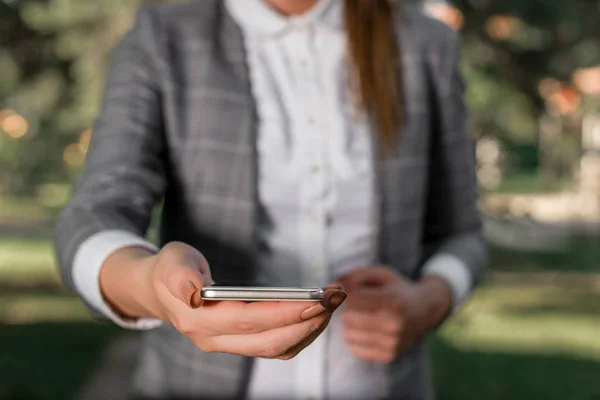 Woman in grey suites holds mobile phone. Business concept with business woman holding mobile phone with touch screen.