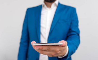 İşadamı elinde tur üst tutar. Dokunmatik ekranlı cep telefonu tutan adam ile iş konsepti. Mavi süitteki işadamı elinde cep telefonuyla duruyor.