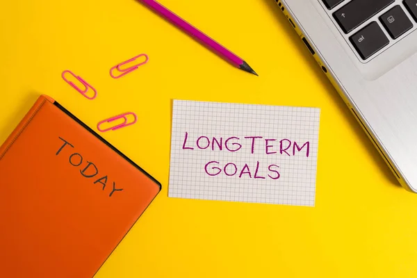Handwriting text writing Longterm Goals. Concept meaning Strategic target that is required more time for completion Laptop clips pencil paper sheet hard cover notebook colored background. — Stock Photo, Image