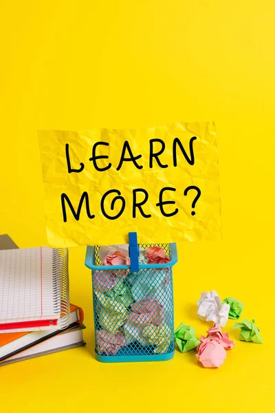 Conceptual hand writing showing Learn More question. Business photo showcasing gain knowledge or skill studying practicing Trash bin crumpled paper clothespin office supplies yellow.