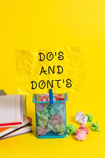 Conceptual hand writing showing Do S Is And Dont S Is. Business photo showcasing advising Rules or customs concerning some activity Trash bin crumpled paper clothespin office supplies yellow.