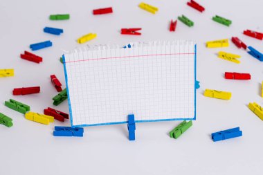 Beyaz bir zeminin ortasında boş dikdörtgen kare şeklinde hatırlatma notu etrafında yerleştirilen renkli clothespin. Ofis malzemeleri, bir bağlantı elemanı tarafından sabitlenmiş boş kağıt.