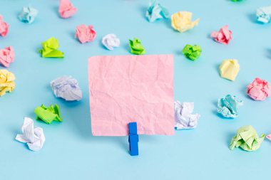 Mavi arka planda boş dikdörtgen kare şeklinde hatırlatma notu etrafında yerleştirilen renkli buruşuk levhalar. Ofis malzemeleri, bir bağlantı elemanı tarafından sabitlenmiş boş kağıt.