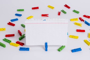 Beyaz bir zeminin ortasında boş dikdörtgen kare şeklinde hatırlatma notu etrafında yerleştirilen renkli clothespin. Ofis malzemeleri, bir bağlantı elemanı tarafından sabitlenmiş boş kağıt.