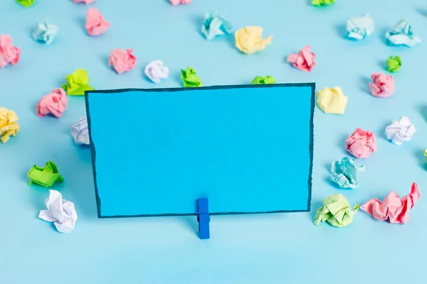 Folhas de crumpled coloridas colocadas em torno da nota de lembrete em forma quadrada retangular vazia no fundo azul. Material de escritório, papel em branco fixado por um fixador . — Fotografia de Stock