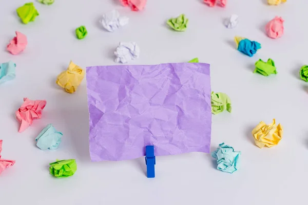 Folhas de crumpled coloridas colocadas em torno da nota de lembrete em forma quadrada retangular vazia no centro de um piso branco. Material de escritório, papel em branco fixado por um fixador . — Fotografia de Stock