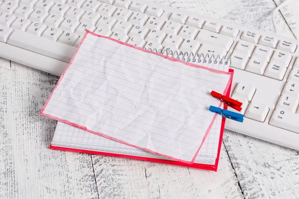 Vierkante papieren notitieboekje met een rechthoek vormige lege notitie boven vastgemaakt door twee wasknijpers op het blad. Wit toetsenbord onder een beurt en lichte houten vloer achtergrond. — Stockfoto