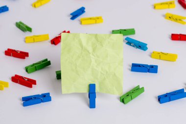 Beyaz bir zeminin ortasında boş dikdörtgen kare şeklinde hatırlatma notu etrafında yerleştirilen renkli clothespin. Ofis malzemeleri, bir bağlantı elemanı tarafından sabitlenmiş boş kağıt.