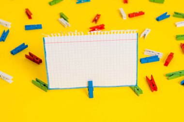Sarı bir arka plan ortasında boş dikdörtgen kare şeklinde hatırlatma notu etrafında yerleştirilen renkli clothespin. Ofis malzemeleri, bir bağlantı elemanı tarafından sabitlenmiş boş kağıt.